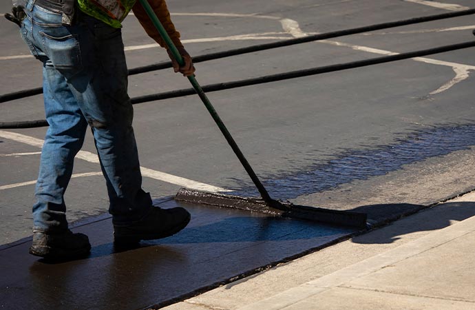 Worker applying seal coating to an asphalt road for protection and longevity.